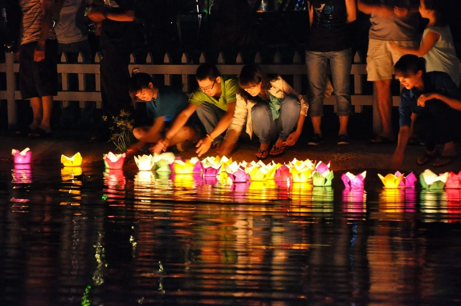Tourists releasing colorful paper flower lanterns onto the Hoai River during the night in Hoi An Ancient Town