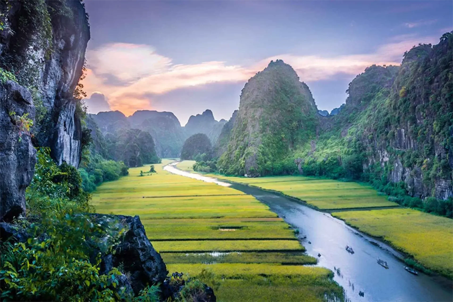 A local woman rowing a traditional sampan boat with her feet along the Ngo Dong River in Tam Coc, Ninh Binh.