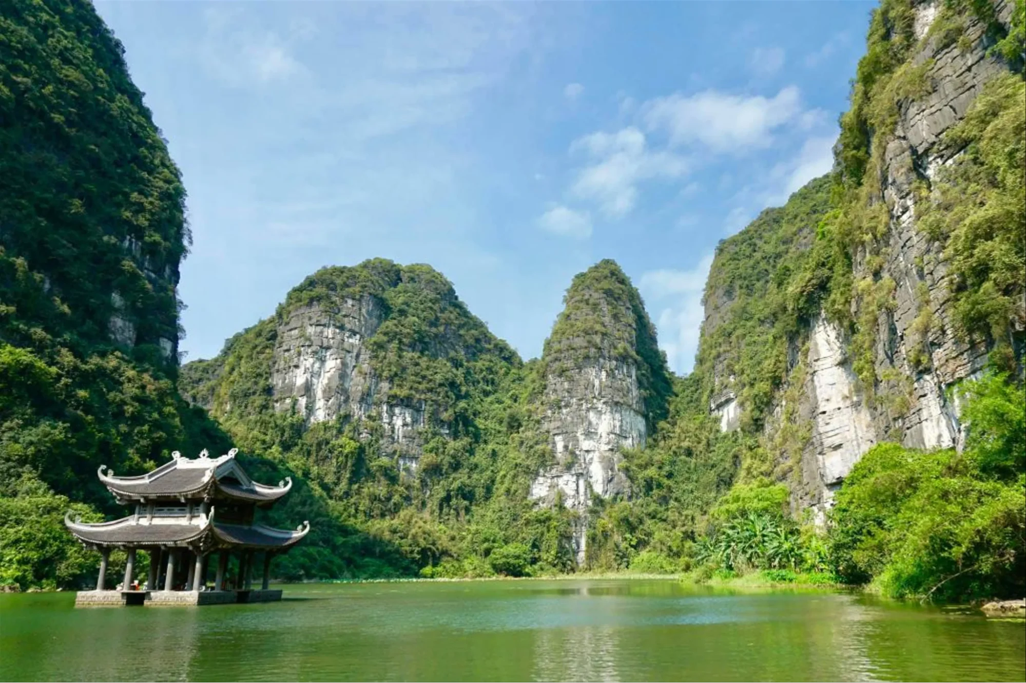 The serene green waters and temple architecture nestled at the foot of limestone cliffs in Trang An UNESCO World Heritage Site.