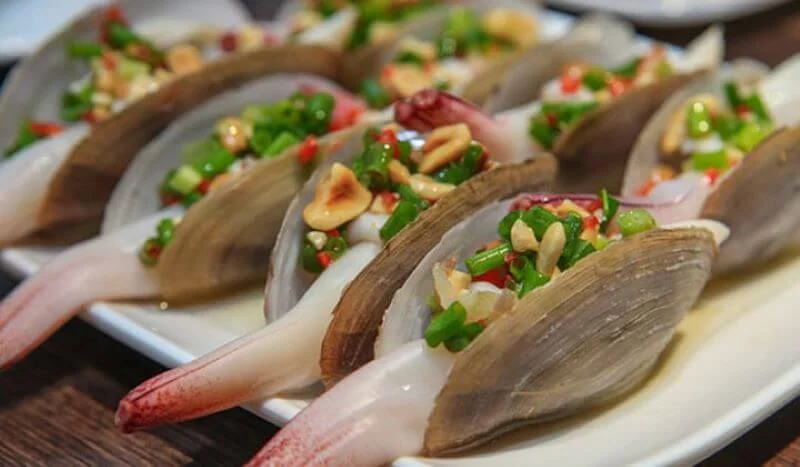 A plate of steamed geoduck garnished with herbs and garlic, a famous seafood dish on Cat Ba Island.