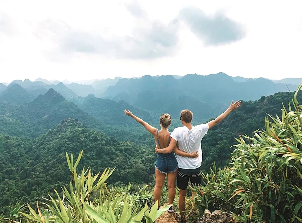 A traveler looking out over the lush green karst mountains of Cat Ba from a high viewpoint.