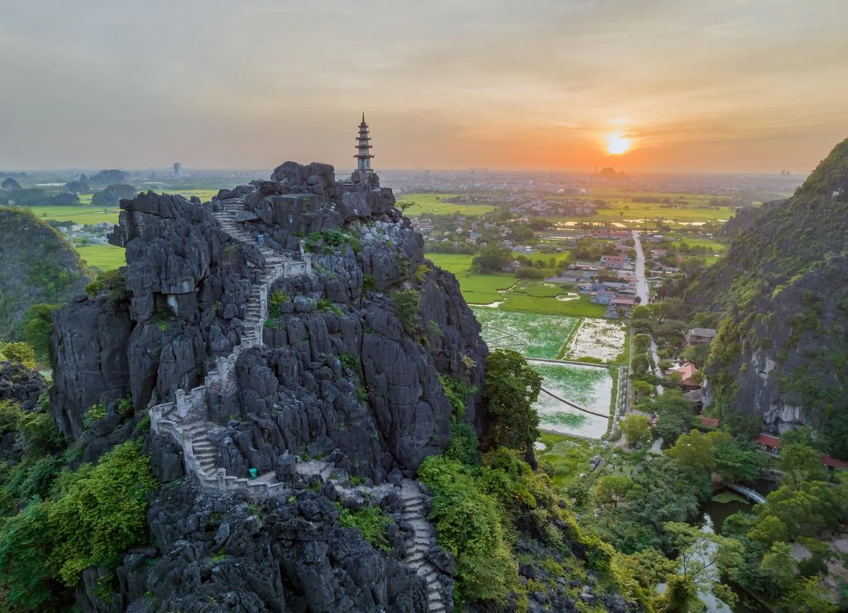 A traveler looking out over a spectacular valley of limestone mountains and yellow rice paddies from the Mua Cave viewpoint.