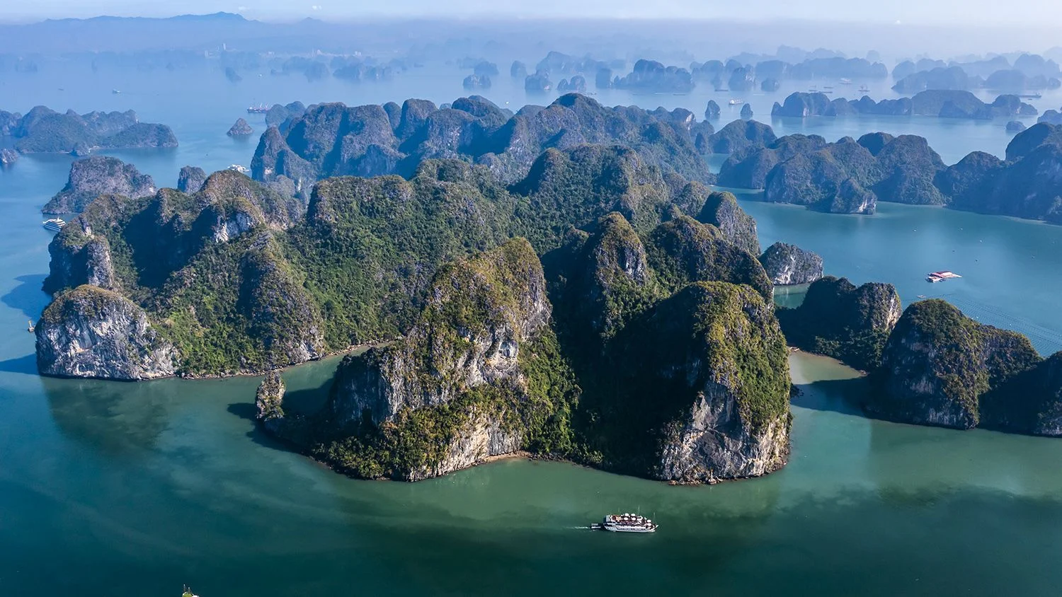 Cat Ba Package Tour featuring a breathtaking panoramic view of green-topped limestone karst islands and traditional cruise ships in Ha Long Bay.