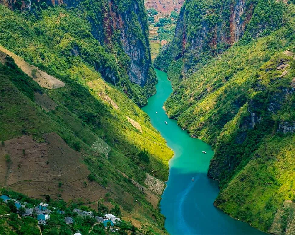 A small boat navigating the turquoise Nho Que River between towering limestone cliffs in Ha Giang.