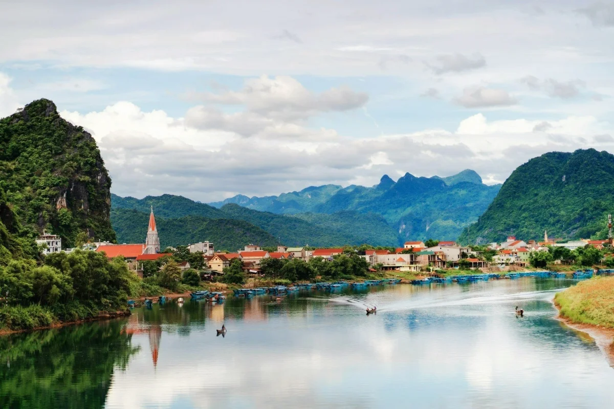 Traditional blue wooden boats drifting along the Son River beneath towering green karst mountains in Phong Nha–Ke Bang National Park.