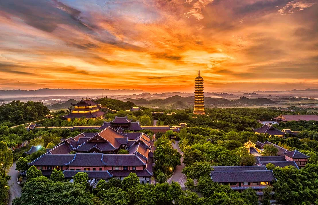 The vast Bai Dinh Pagoda complex in Ninh Binh featuring towering Buddha statues, stone Arhat corridors, and misty limestone hills in the background.