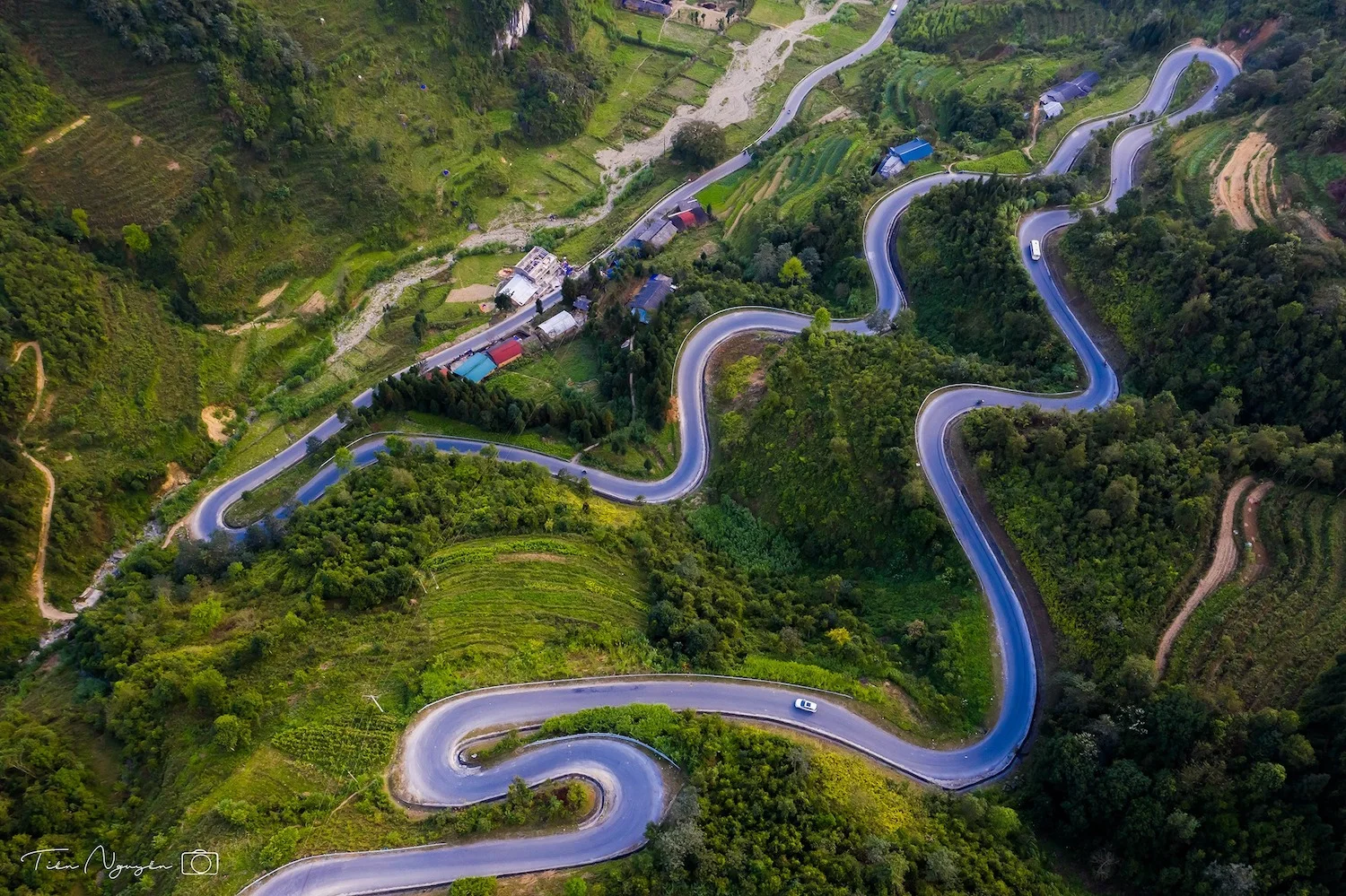 A sweeping aerial view of Ma Pi Leng Pass with serpentine mountain roads and dramatic limestone valleys in Ha Giang.