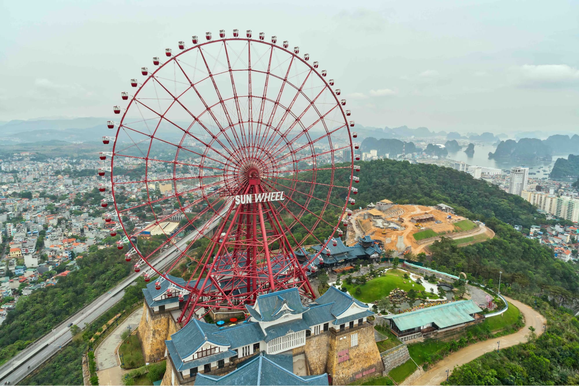 The giant Sun Wheel illuminated at night, overlooking the Bai Chay Bridge and Ha Long city skyline.